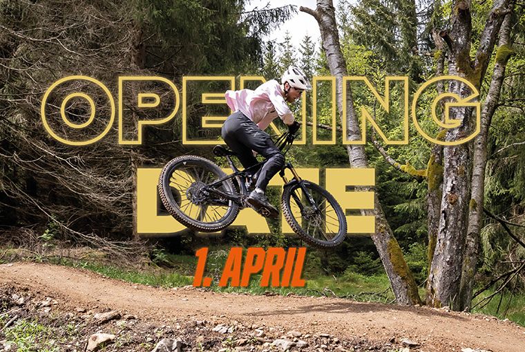 1. April: Opening Date TrailCenter Rabenberg Mountainbiker springt über eine Schanze mit Text "OPENING DATE 1. APRIL" im Wald.