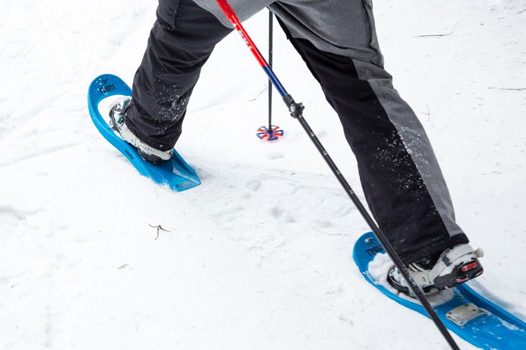 Rabenberg Sportkurse: Schneeschuhtour Das Bild zeigt eine Person, die Schneeschuhe in tiefem Schnee trägt. Die Person trägt dunkle Hosen und weiße Schuhe. Die Schneeschuhe sind blau. In der Szene sind auch Skistöcke vorhanden.